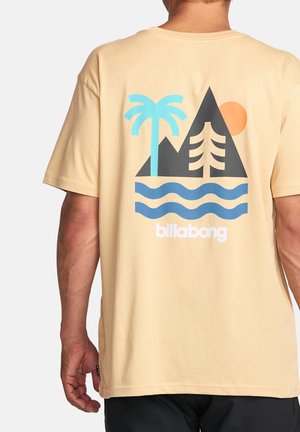 Beige bomull t-skjorte med grafisk trykk som viser fjell, et palmetre, bølger og en sol; "Billabong" logo i hvitt nederst.