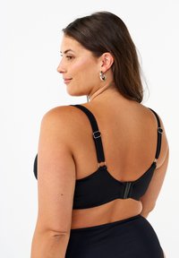 Reggiseno nero con spalline regolabili, texture liscia e chiusura con gancetto sul retro, progettato per comfort e supporto.