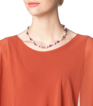 Purple and white beaded necklace featuring various shapes with smooth and textured surfaces, worn on a model with an orange top.