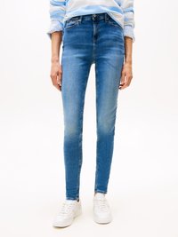 Jeans ajustados de mezclilla azul medio con un lavado desgastado, cintura alta, diseño de cinco bolsillos y cierre de cremallera, combinados con zapatillas blancas.