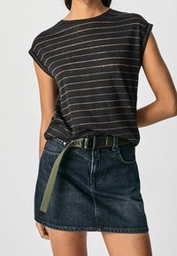 Sort stribet t-shirt med korte oprevne ærmer, båret med en mørk denimnederdel og et olivengrønt bælte. Har subtile metalliske striber.