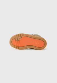 Semelle de chaussure avec une base en caoutchouc gum, présentant un motif de bande rayé orange et de légères rainures pour l'adhérence, avec une surface texturée.