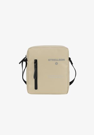 Béžová crossbody taška vyrobená z hladkého syntetického materiálu, s černým zipem, nastavitelným popruhem, embosovaným logem značky a vytištěnými souřadnicemi.