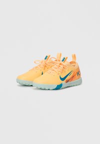 Zapatillas deportivas de color naranja claro con acentos azules, parte superior texturizada y una suela flexible y translúcida con un diseño de dibujo en suela.