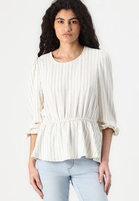 Blouse rayée blanche avec un col rond, des manches bouffantes et une taille élastique pour une silhouette peplum. Texture de tissu lisse.