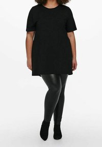 Svart kortärmad tunika i mjukt tyg, kombinerad med glänsande svarta leggings och svarta ankelstövlar. Enkla, avslappnade passform.