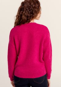 Pull en peluche, de couleur rose vif, avec une coupe décontractée, un col rond et des manches longues. Un ourlet et des poignets côtelés ajoutent de la texture. Vue arrière montrée.