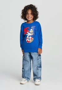 Felpa blu con grafica di Sonic the Hedgehog, abbinata a jeans cargo azzurri e sneakers bianche.