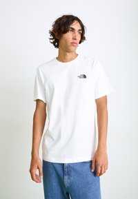 T-shirt alb din bumbac, cu mâneci scurte și decolteu rotund. Prezintă un mic logo negru pe partea stângă a pieptului. Pur și simplu, este asortat cu blugi albaștri.