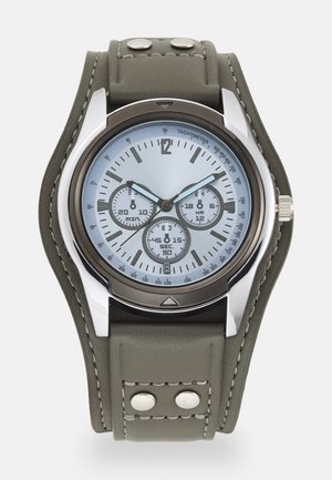 Montre argentée avec un cadran bleu, trois sous-cadrans et des marquages tachymétriques. Équipée d'un bracelet en cuir vert avec des clous argentés.