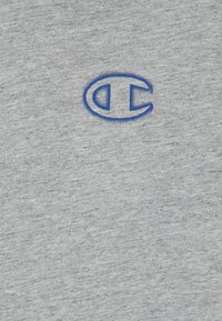 Pelēks sporta krekls ar teksturētu audumu. Uz krūtīm ir zils izšūts logotips. Vienkārša apkakles dizaina forma. Mīksts un ērts.