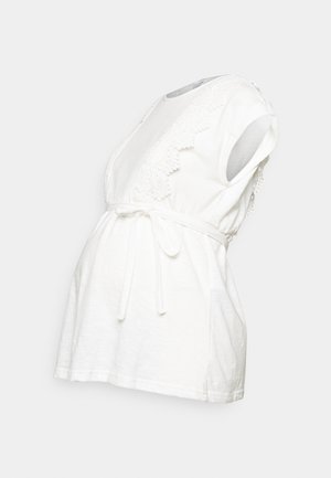 Balta nėštumo palaidinė, pagaminta iš minkštos medvilnės, su apvyniojimo dizainu, trumpomis rankovėmis, nėriniuotais akcentais pečių srityje ir surišamu juosmeniu, leidžiančiu reguliuoti dydį.