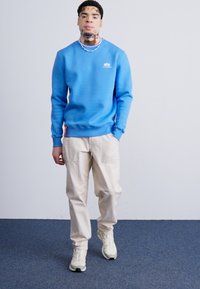 Lys blå sweatshirt med ribbede manchetter, parret med beige cargo bukser med sidelommer. Model iført neutrale sneakers.