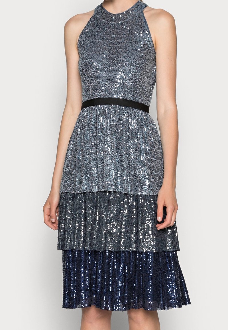 Abito senza maniche con collo all'americana, decorato con paillettes argento e blu, design a strati, corpetto aderente e cintura nera in vita.