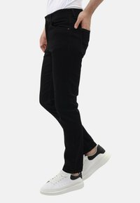 Zwarte denim jeans met een slim fit, voorzien van zilveren hardware, voor- en achterzakken, gecombineerd met witte sneakers met zwarte accenten.