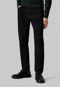 Pantaloni in denim nero con una vestibilità slim, dotati di tasche anteriori e design classico. Indossati con scarpe nere per un look coerente.