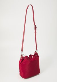 Piros nylon táska húzózsinórral és ezüst színű fémrészletekkel, egy állítható pánttal és puha, sima felülettel.