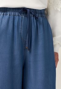 Pantalon en denim bleu avec une taille élastique et un cordon de serrage. Présente une coupe droite et des détails de couture subtils.