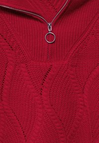 Roter Strickpullover mit einem Reißverschlusskragen, der ein strukturiertes Wellenmuster und einen runden silbernen Reißverschluss-Zieher aufweist.