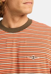 Stribet t-shirt i orange, creme og brun; har en rund halsudskæring og broderet logodetalje på brystet. Blødt bomuldsstof.