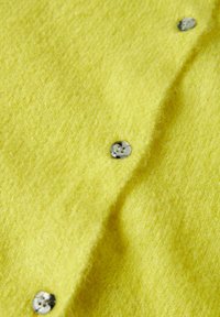 Kollane kootud kangas pehme tekstuuriga, millel on ümmargused, läbipaistvad nupud, mis lisavad disainile detaili.