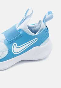 Baskets de sport bleues avec tige en synthétique, accents blancs, sangle élastique au niveau du milieu du pied, maille respirante et boucle renforcée au talon pour un enfilage facile.