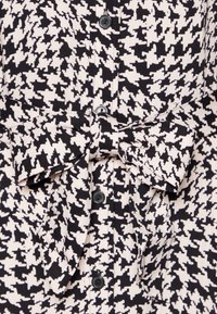 Tkanina w wzór houndstooth w czerni i bieli z guzikami oraz kokardą w talii. Teksturowany materiał bawełniany.