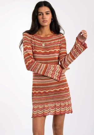 Vestido de punto con un patrón en zigzag en tonos cálidos de rojo, rosa y beige. Mangas largas con puños acampanados y un dobladillo con forma de onda.