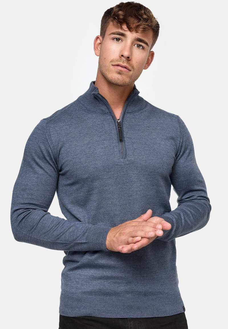 Pull over zippé léger de couleur bleu foncé, doté d'un col montant et de poignets côtelés. Texture lisse avec une coupe ajustée.
