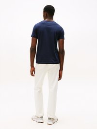 Mørkeblå crew neck t-shirt, korte ærmer, afslappet pasform, parret med hvide lige ben jeans og hvide sneakers med grå detaljer.