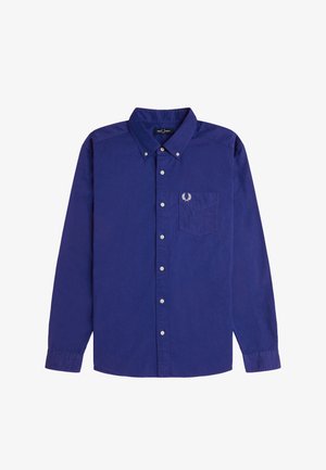 Pitkähihaiset, napilliset tummansiniset paita, jossa on kaulus ja rintatasku, jossa on pieni valkoinen kirjailtu logo.