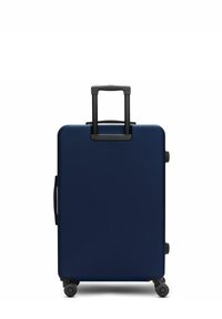 Valigia rigida blu navy con manico telescopico nero e quattro ruote rotanti, in posizione verticale su uno sfondo bianco.