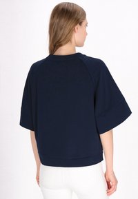 Felpa corta blu navy con maniche ampie e scollo rotondo, realizzata in tessuto morbido, caratterizzata da una vestibilità rilassata e dettagli di cucitura discreti.