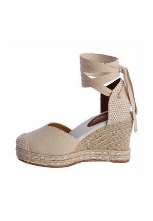 Zapato espadrille beige con cuña, suela de yute trenzado, punta cerrada y lazos de tela que se atan alrededor del tobillo y hacen un lazo en la parte trasera.