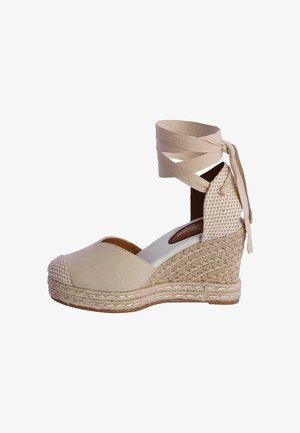Zapato espadrille beige con cuña, suela de yute trenzado, punta cerrada y lazos de tela que se atan alrededor del tobillo y hacen un lazo en la parte trasera.