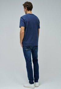 Camiseta de algodón azul marino de manga corta, combinada con jeans azul oscuro y zapatillas blancas. Vista desde atrás, mostrando la textura de la tela.