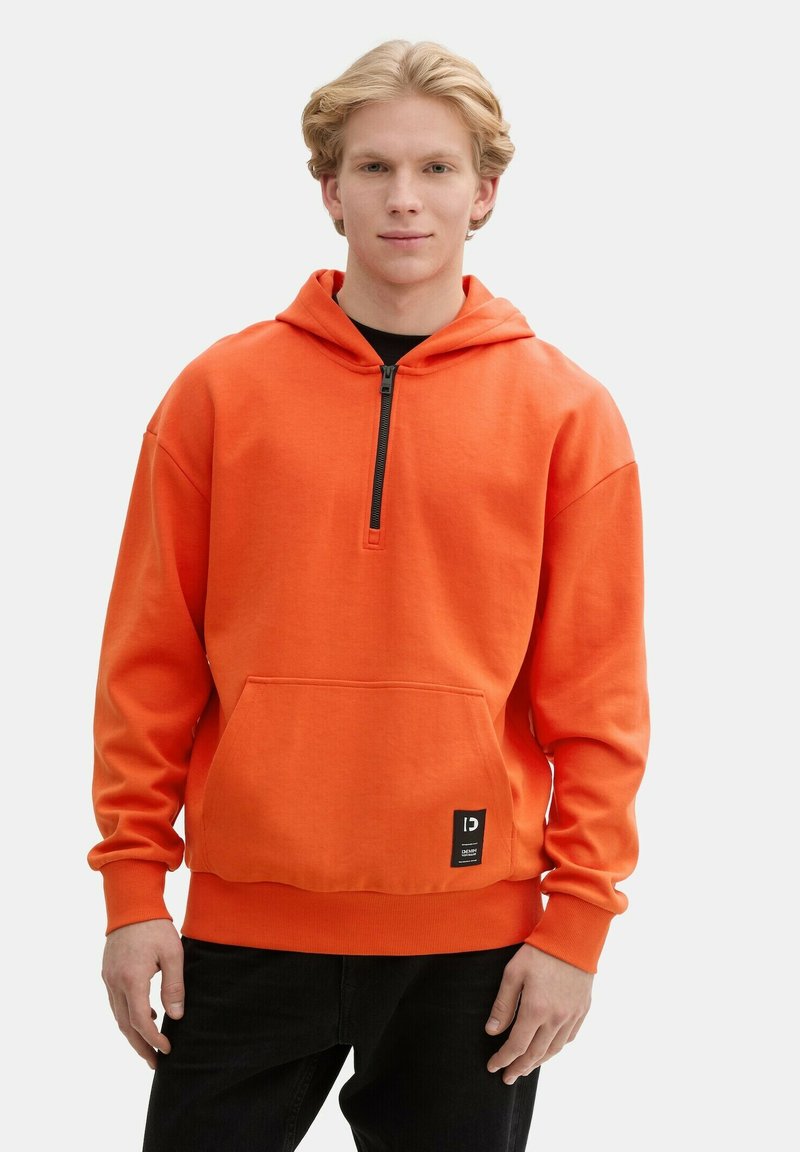 Sudadera naranja con bolsillo frontal, escote con media cremallera y puños acanalados. Presenta una etiqueta en el dobladillo, hecha de tela suave.