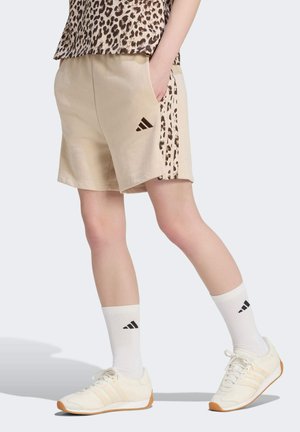Persona che indossa pantaloncini beige con strisce a stampa leopardata, camicia con stampa leopardata abbinata, calzini bianchi Adidas e sneakers beige Adidas.