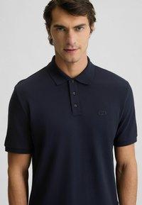 Polo shirt blu navy realizzato in tessuto morbido, con colletto classico, placket a tre bottoni e un discreto accento del logo sul lato sinistro del petto.