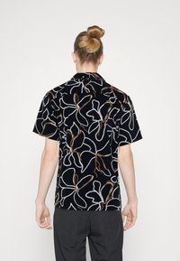 Krátký rukáv košile z černé látky s květinovým vzorem v bílé a hnědé barvě, s pohodlným střihem a špičatým límcem.