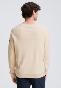 Gaiši bēša adīta džempera ar garām piedurknēm, ribotiem aproču galiem un apaļu kakla izgriezumu. Mīksta tekstūra un brīvs piegriezums. Piedurknes vietā iekļauta zīmola birka.