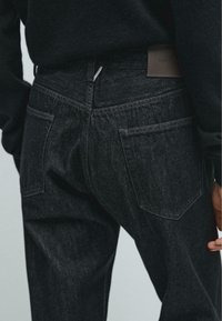 Jeans in denim scuro con tasche posteriori classiche, dettagli di cucitura discreti e un'etichetta in pelle in vita. Tessuto testurizzato evidente.