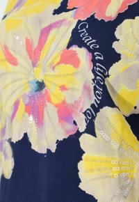 Tissu avec de grandes impressions florales jaunes et roses, des paillettes argentées, et la phrase « Créez une vie que vous aimez » sur un fond bleu foncé.