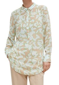 Blusa trasparente beige con motivo astratto di foglie bianche e verdi, maniche lunghe, colletto con bottoni e orlo arrotondato. Texture liscia.