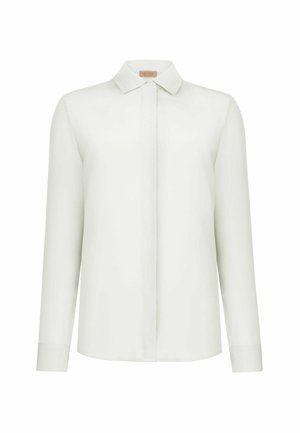 Blusa bianca a maniche lunghe con chiusura frontale con bottoni nascosti, collo a punta e orlo dritto, esposta su sfondo bianco.