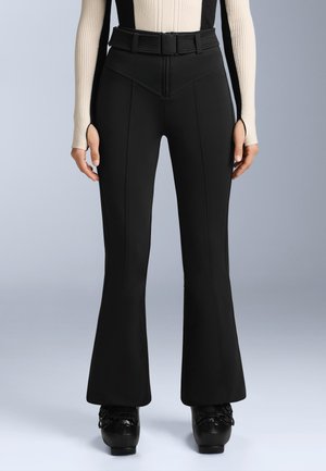 Crne traperice s flared krojem izrađene od rastezljivog materijala, s prednjim šavovima, visokim strukom i petljama za remen. U paru s crnim platformama.