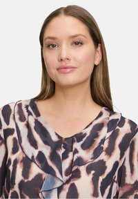 Chemisier transparent avec un imprimé léopard dans des teintes de marron et de crème, doté d'un col froncé et d'une texture douce et fluide.