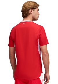 Rotes Sporttrikot mit weißen Akzenten, kurzen Ärmeln, strukturierter Stoff und rundem Halsausschnitt. Mit "suisse"-Logo auf der Rückseite.