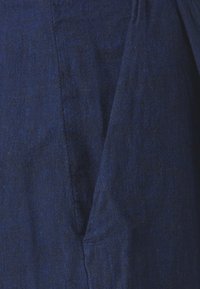 Țesătură de in de culoare albastră închisă cu o suprafață texturată, având pliuri și cusături, indicând un design structurat și un stil casual.