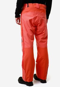 Pantaloni impermeabili arancioni con finitura texturizzata, dotati di una vita alta e tasche laterali. Sezioni inferiori rinforzate per maggiore durata.